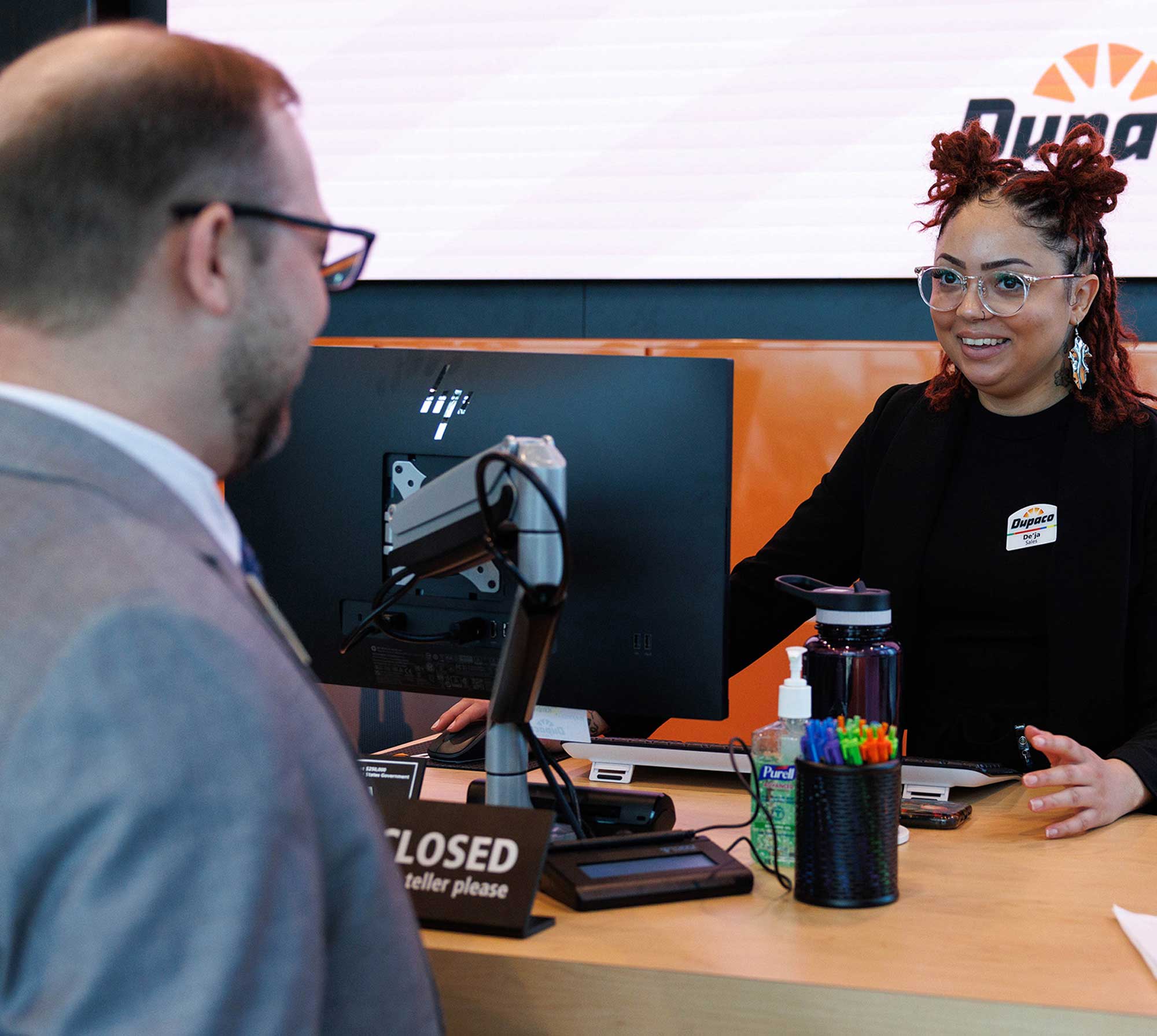 A woman behind a bank counter assists a man standing in front of her.